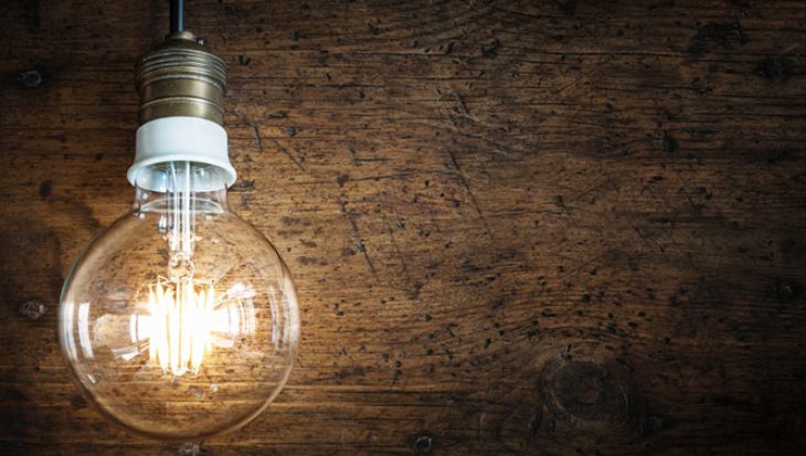 A lit lightbulb hanging against a wood panel.